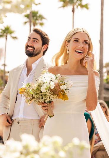 A radiant bride and groom smiling joyfully at their sunny outdoor wedding ceremony.